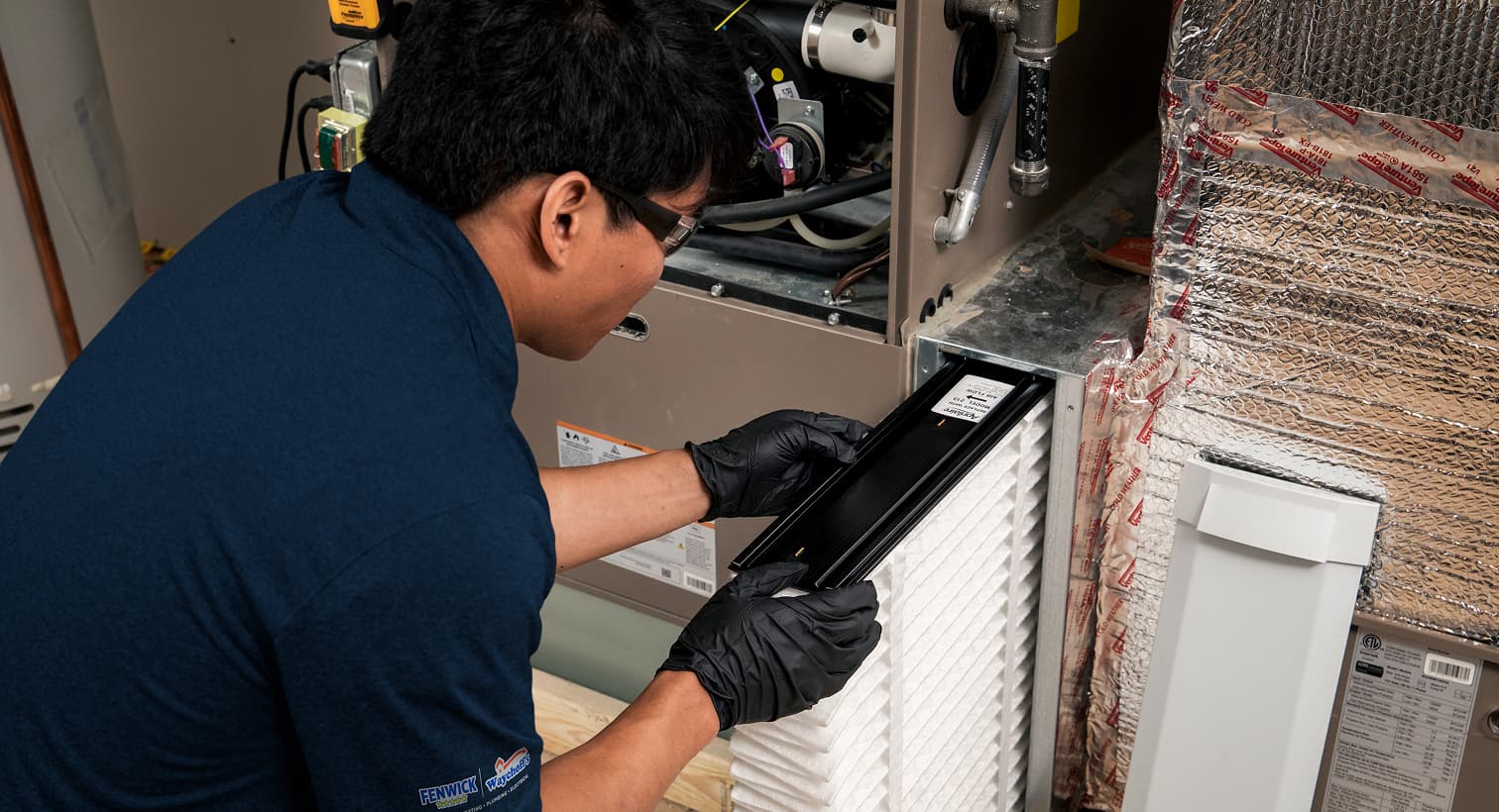 A professional Fenwick Waychoff's HVAC technician replacing a clean pleated air filter in an indoor air handler unit during a routine AC maintenance tune-up.