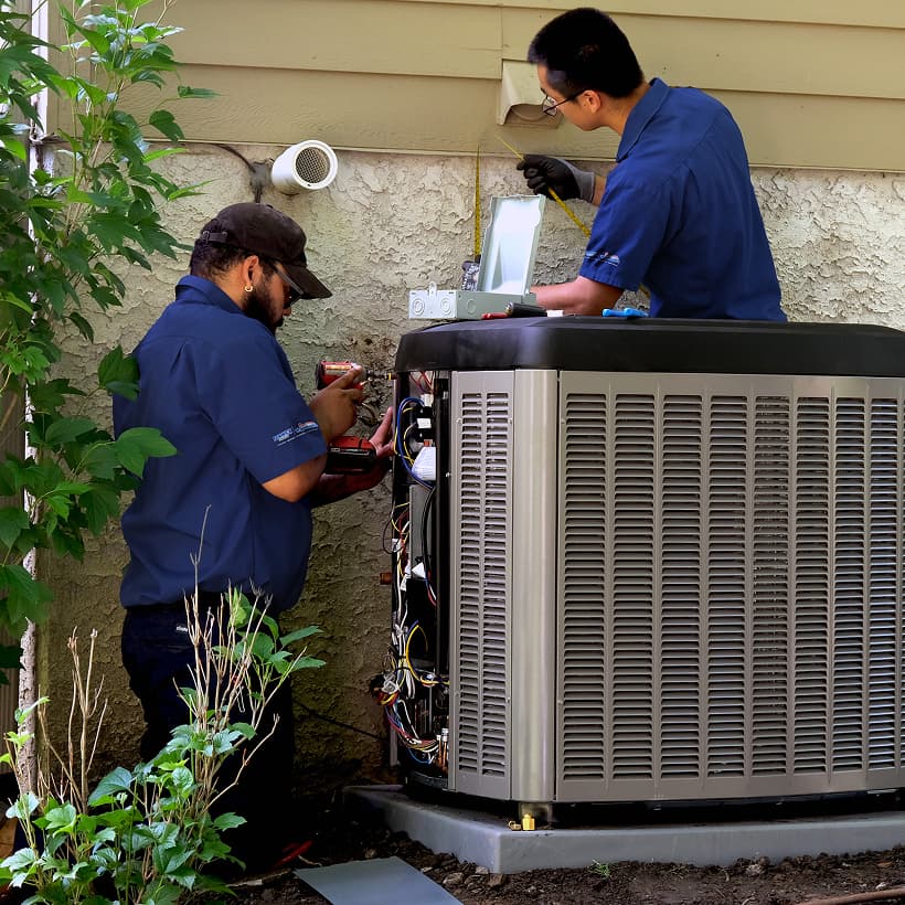 Two Fenwick Waychoff's HVAC technicians installing a brand-new residential outdoor air conditioning condenser unit during a home AC replacement service.