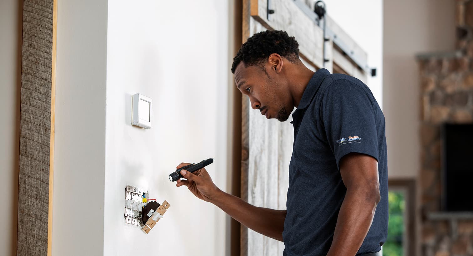 A professional Fenwick Waychoff's electrician using a flashlight to safely inspect and troubleshoot exposed residential wall switch wiring during an electrical repair service.